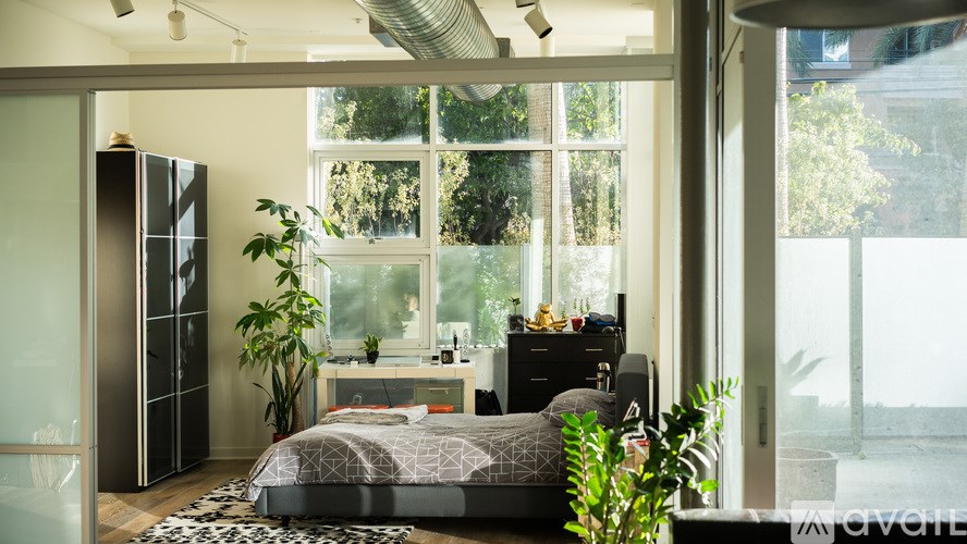 A bedroom with a bed, nightstand, and a window with a view of the city.