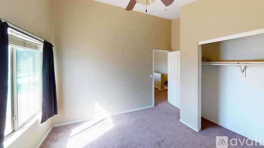 A room with a carpeted floor, a window with black curtains, and a ceiling fan.