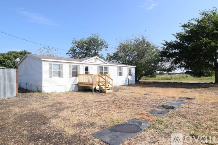 A white mobile home with a porch and a tree in the backyard.