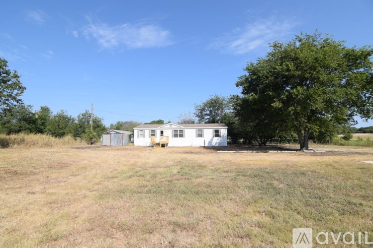 A white house is situated in a field with a tree to the right.