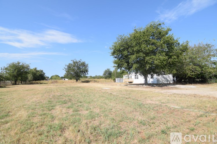 A field with a tree and a white building in the background.