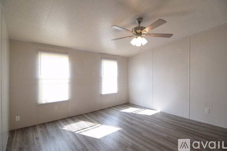 A room with a ceiling fan and two windows.