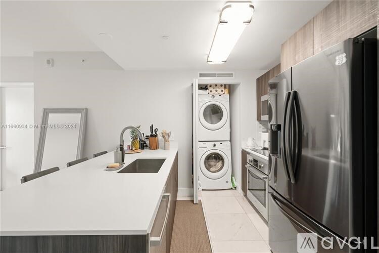 A modern kitchen with a stainless steel refrigerator, a sink, and a washing machine.