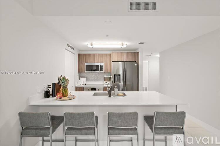 A modern kitchen with a white countertop and grey chairs.