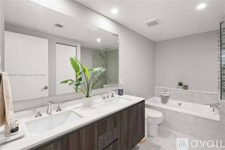 A modern bathroom with a large mirror, a sink, a toilet, and a bathtub.