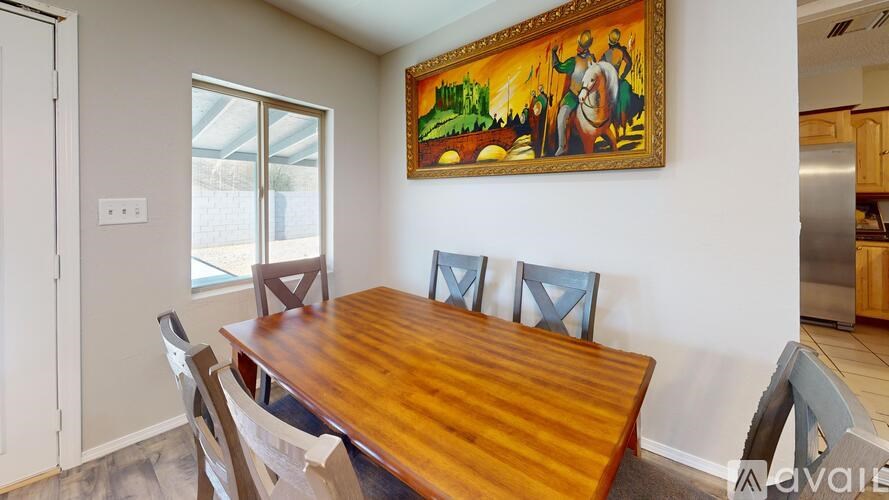 A dining room with a wooden table and chairs and a painting on the wall.