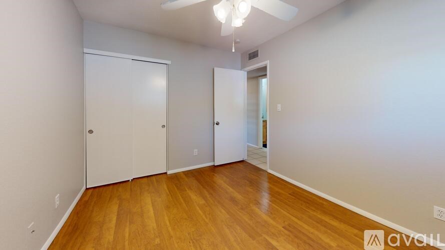 A room with wooden floors and white walls, with a ceiling fan and two doors.