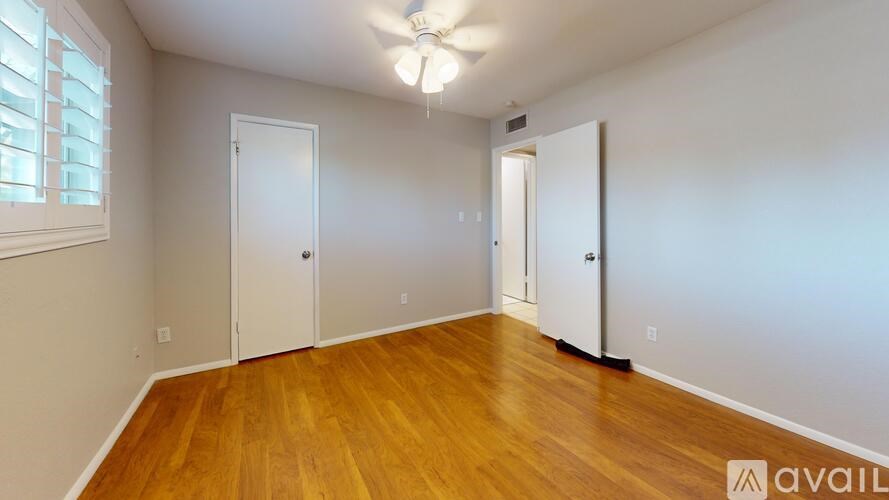A room with wooden floors and white walls, with a ceiling fan and three doors.