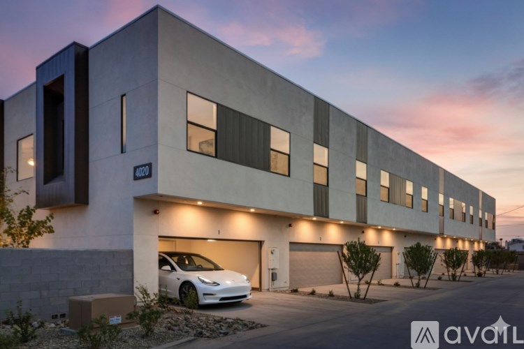 A white Tesla car is parked in front of a modern building with a garage.