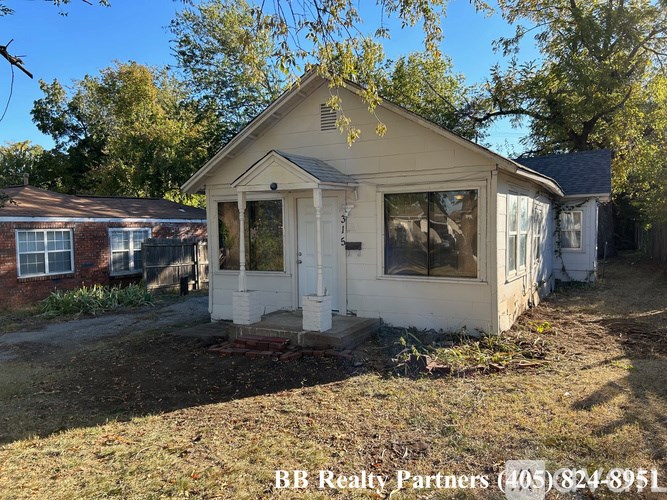 A small house with a white door and windows is surrounded by trees.