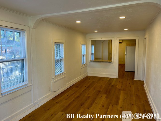 A room with wooden floors and white walls, with a window on the left and a door on the right.