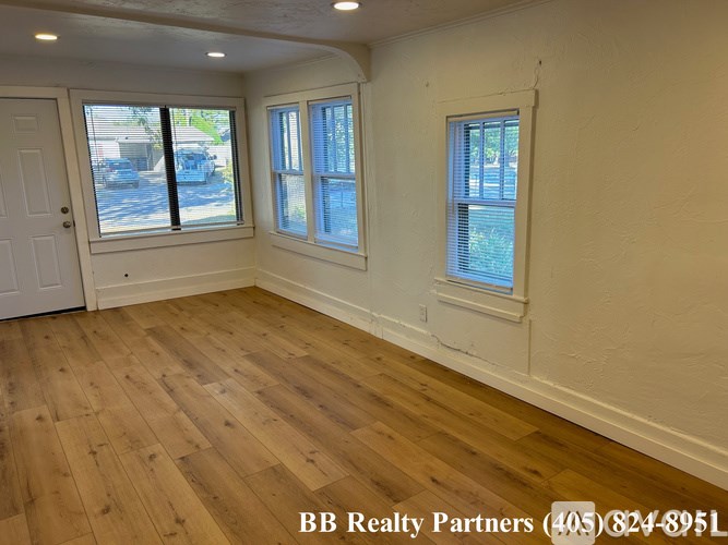 A room with wooden flooring and two windows.