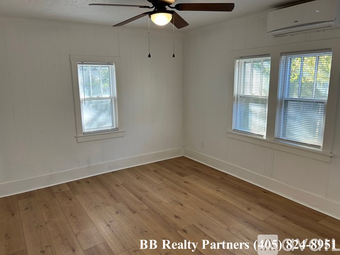 A room with a ceiling fan and two windows.