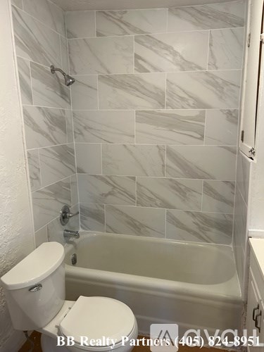 A white toilet sits in a bathroom with a marble tile shower.