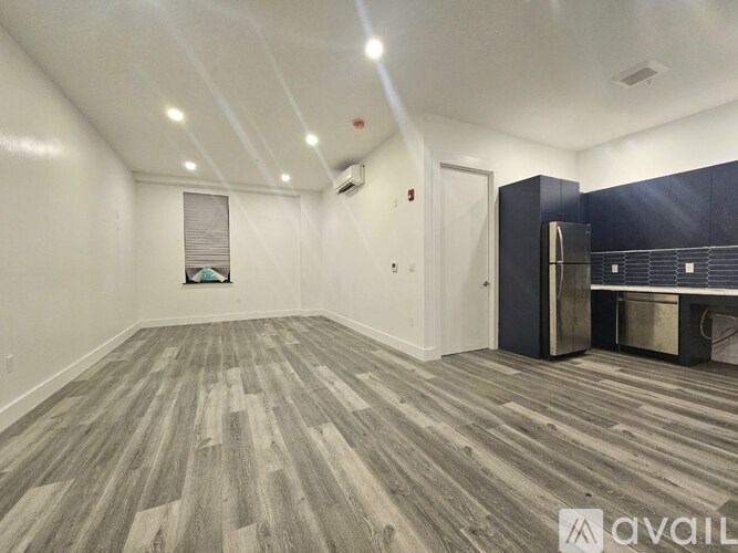 A spacious room with wood flooring and a kitchenette in the corner.