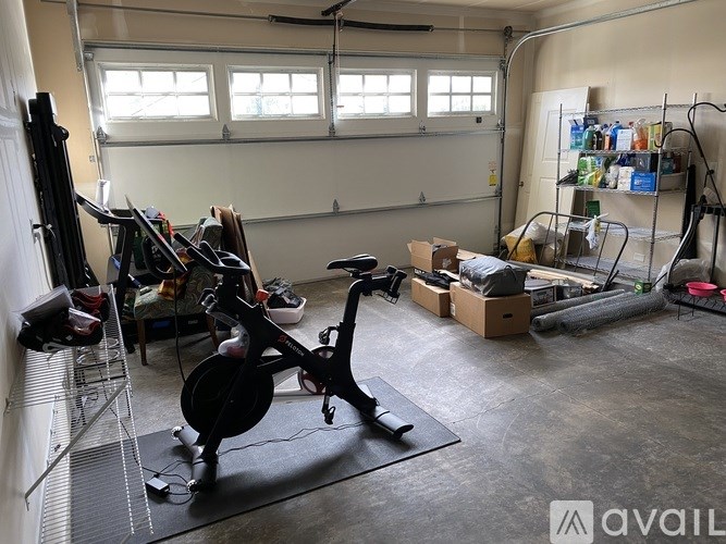 A room with a stationary bike, a rack of shoes, and a wall of shelves with various items.