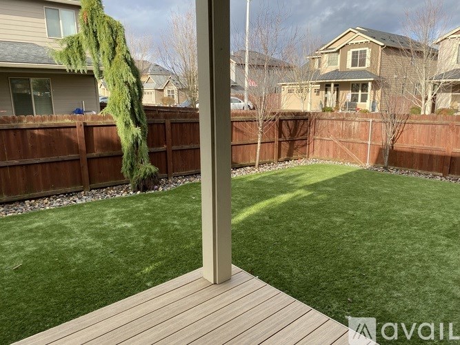 A backyard with a wooden deck and a green artificial lawn.