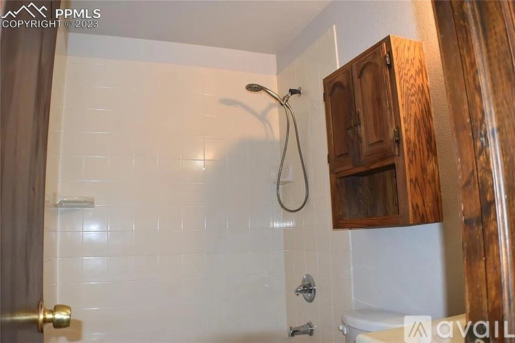 A bathroom with a white tiled shower and a wooden cabinet.