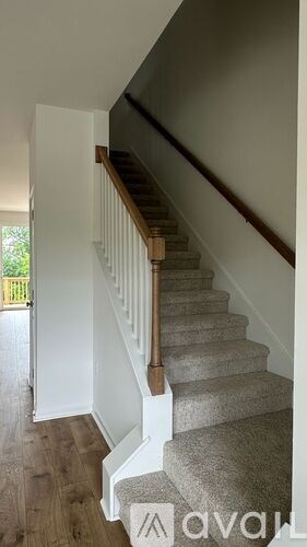 A staircase with a wooden handrail and beige carpeted steps.