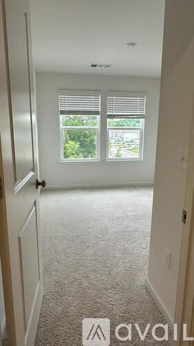 A hallway with a carpeted floor and a window with blinds.