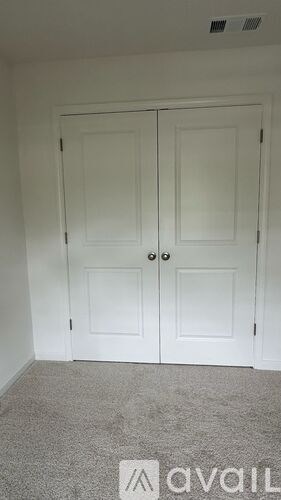 A room with a carpeted floor and a white door with a handle.