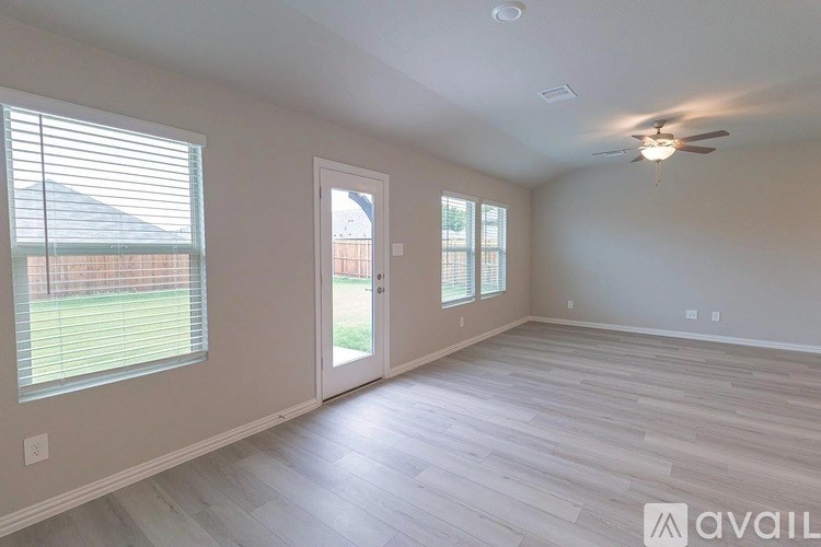 A spacious room with a ceiling fan and light, hardwood flooring, and a door leading to another room.