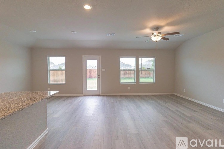 A spacious room with a ceiling fan and lighting fixture, featuring a carpeted area and a hardwood floor.