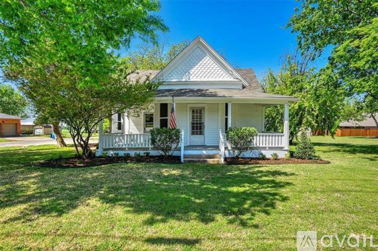 A white house with a porch and a tree in front.