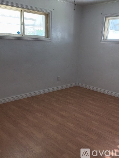 A room with wooden flooring and two windows.