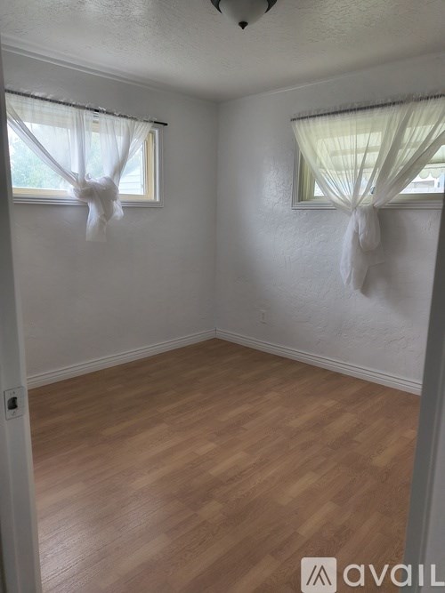 A room with wooden floors and two windows with white curtains.