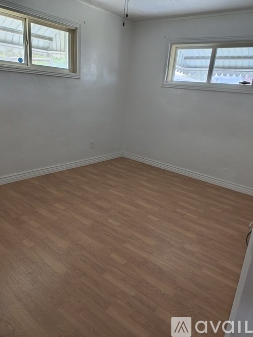A room with wooden flooring and two windows.