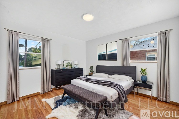 A bedroom with a large bed, a bench, and a window with curtains.