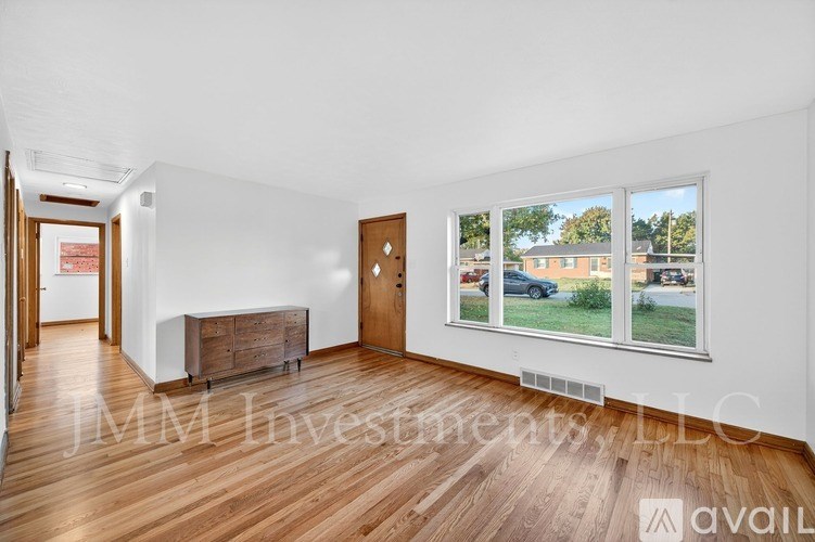 A room with wooden floors and white walls, with a large window showing a view of a building and a car outside.