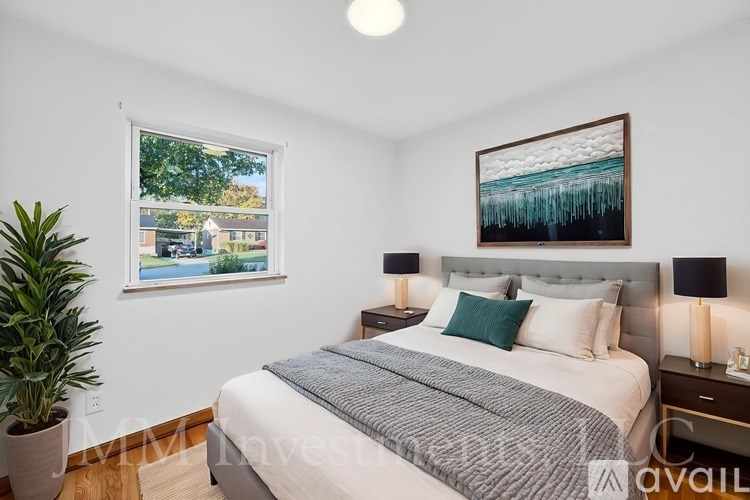 A bedroom with a large bed, a potted plant, and a framed picture on the wall.
