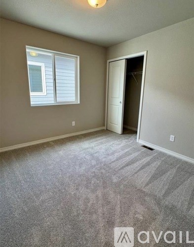 A room with a carpeted floor, a window with blinds, and a door leading to another room.