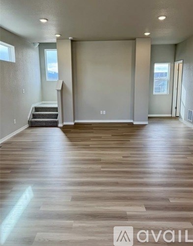 A spacious room with wooden flooring and a staircase leading to another level.