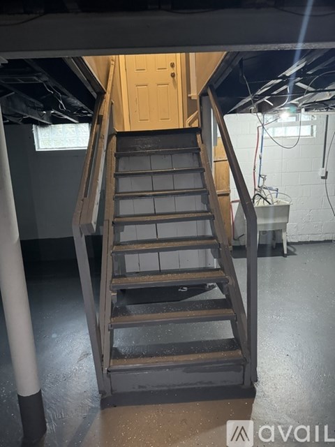 A wooden staircase in a room with a white wall and a door in the background.