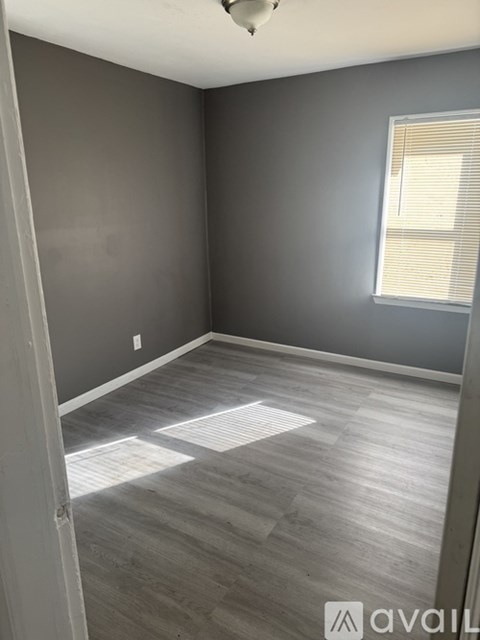A room with grey walls and wooden flooring with a window on the right side.