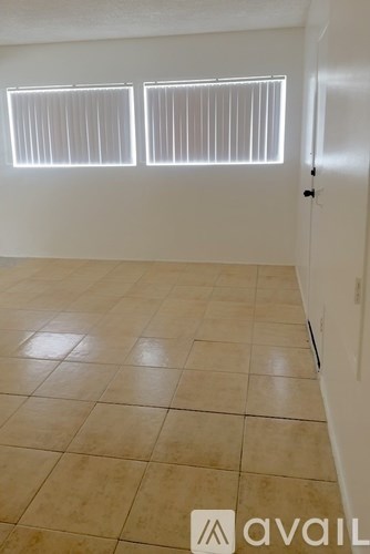 A room with tiled flooring and two windows with blinds.