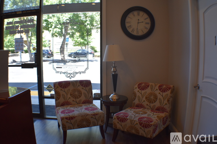 Two chairs with floral patterns sit in front of a window with a view of a street.