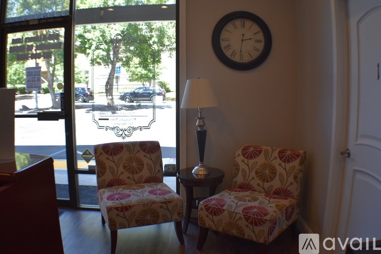 Two chairs with floral patterns sit in front of a window with a view of a street.