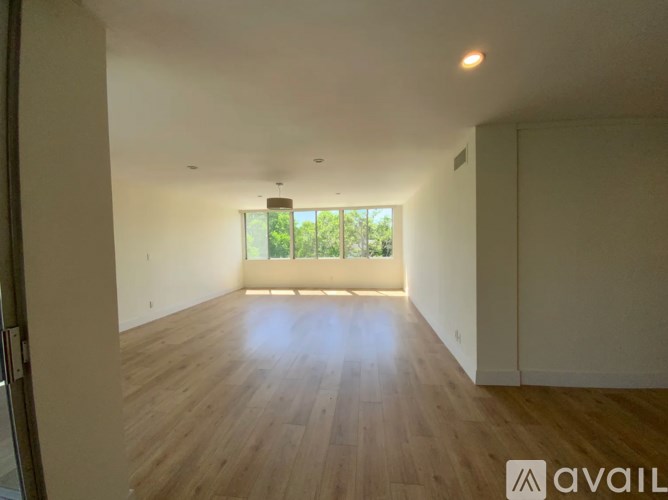 A spacious room with wooden flooring and a window overlooking greenery.