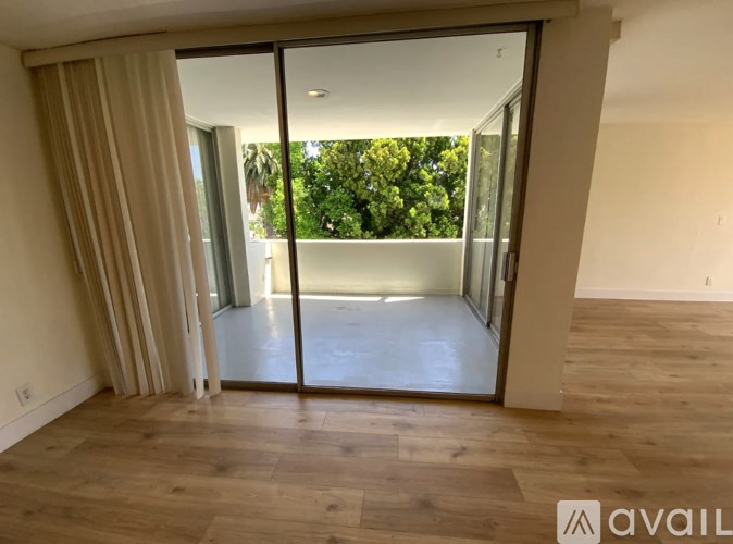A room with wooden flooring and a sliding glass door leading to a balcony.