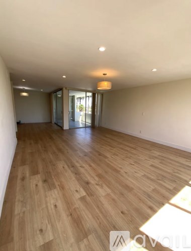 A spacious room with wooden flooring and a sliding glass door.