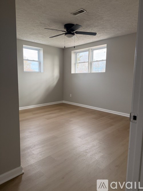 A room with a ceiling fan and two windows.
