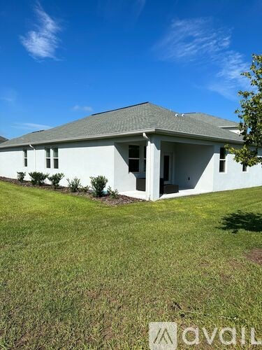 A white house with a grey roof and a tree in front of it.