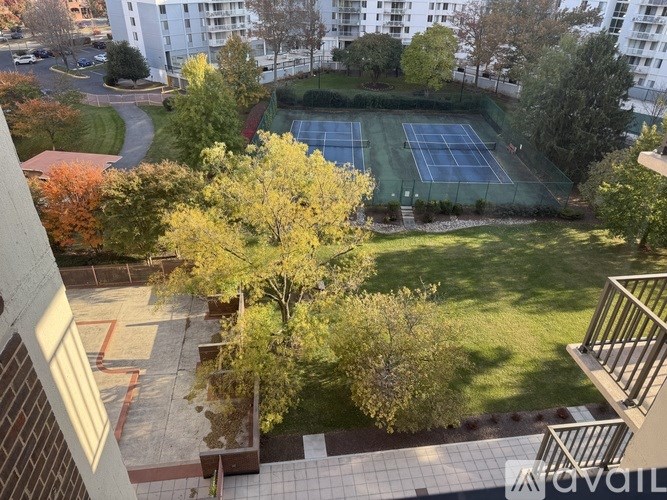 A tennis court is surrounded by trees and grass in a residential area.
