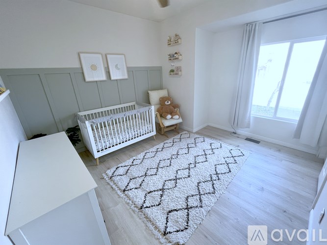 A baby's room with a white crib and a teddy bear on the floor.
