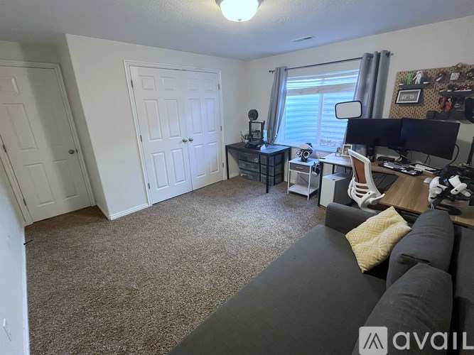 A living room with a grey couch and a black desk with a computer.