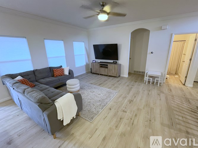 A living room with a grey couch, a white rug, a wooden floor and a ceiling fan.